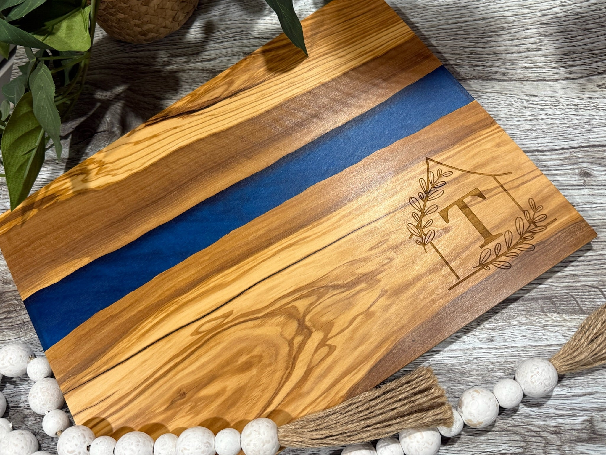 Wooden cutting board with blue resin inlay and engraved monogram on a wooden surface.