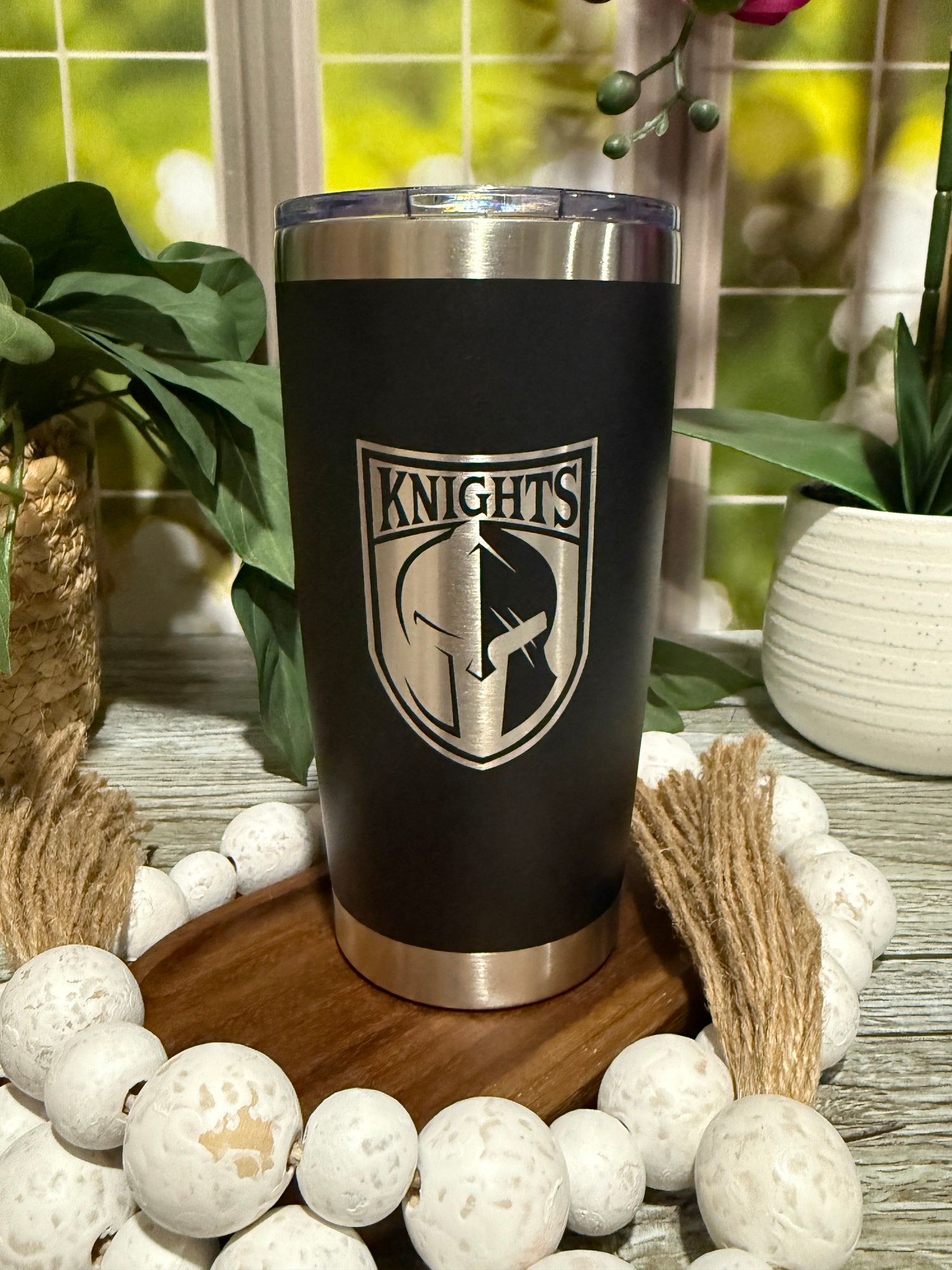 Black 20oz stainless steel tumbler engraved with Canandaigua Knights hockey team logo, staged with wood beads and greenery.