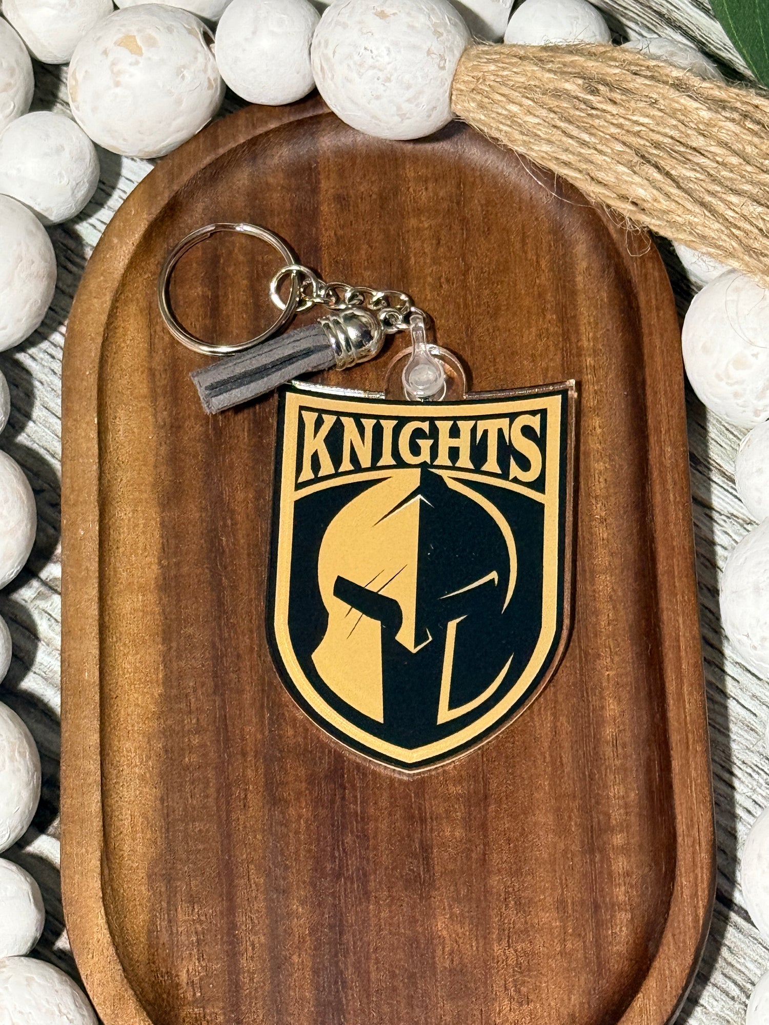 Acrylic keychain featuring the Canandaigua Knights logo, UV printed with optional gray and black tassel, displayed on a wooden tray with decorative beads.