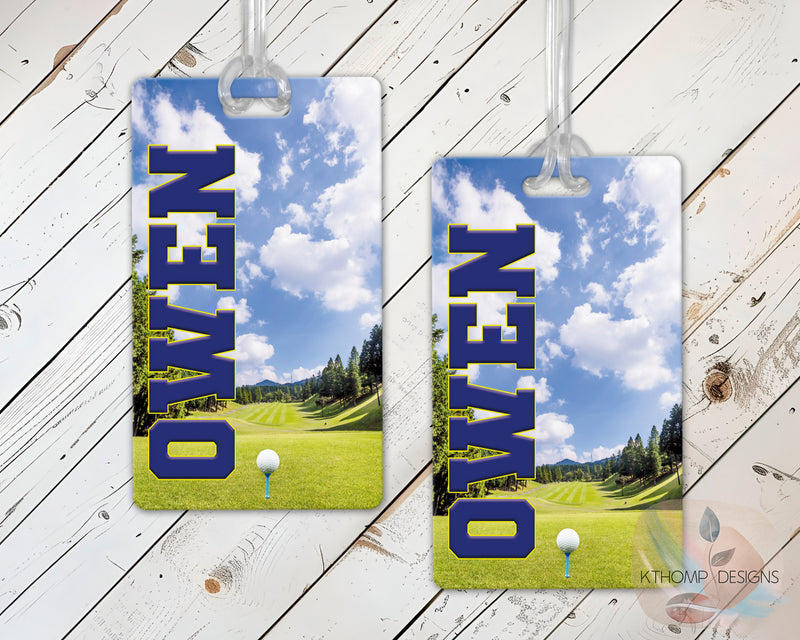 Two luggage tags with a golf course design and a name on a wooden surface.
