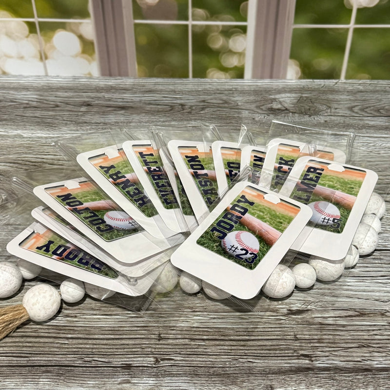 Baseball themed sports bag tags with player names and numbers on a wooden surface.