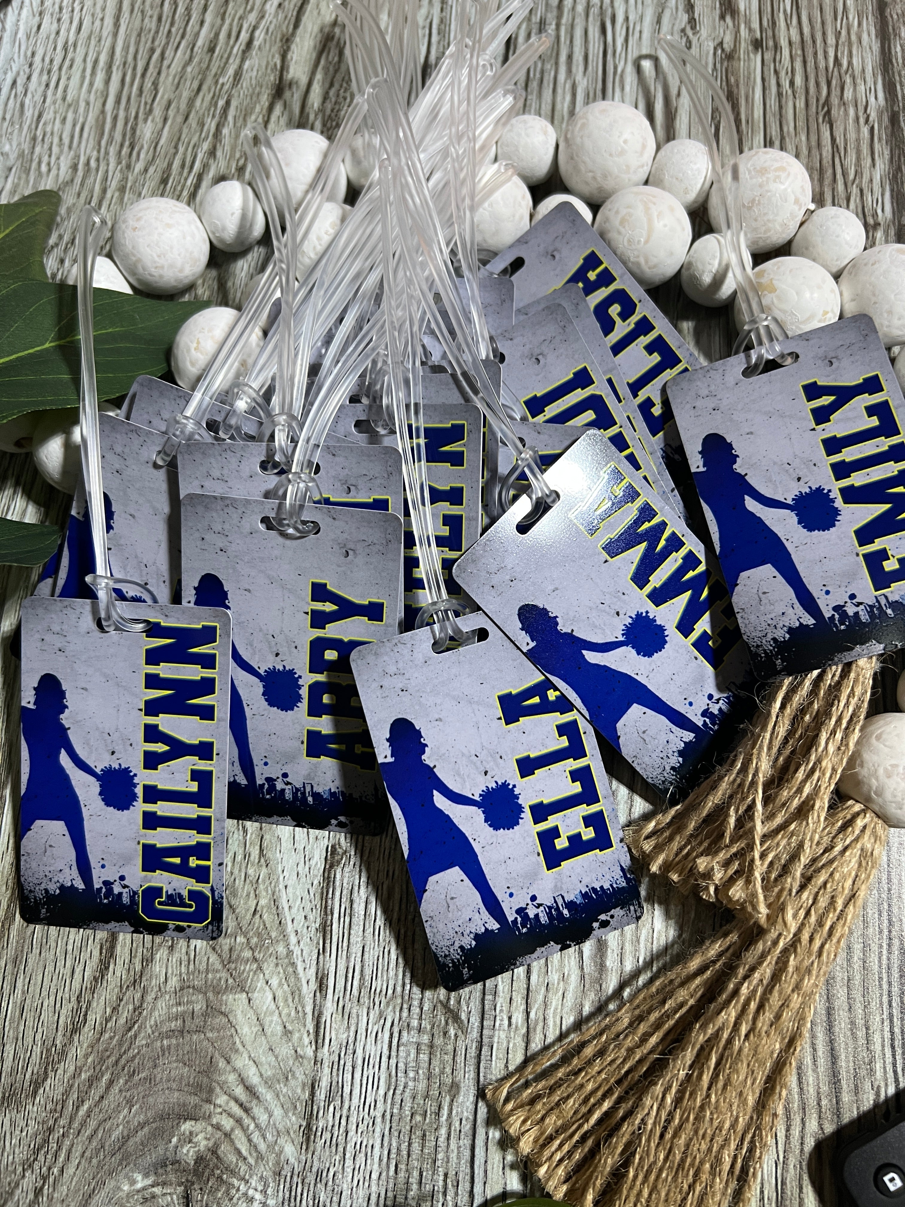 Personalized sports bag tags with blue and white cheerleader designs on a wooden surface