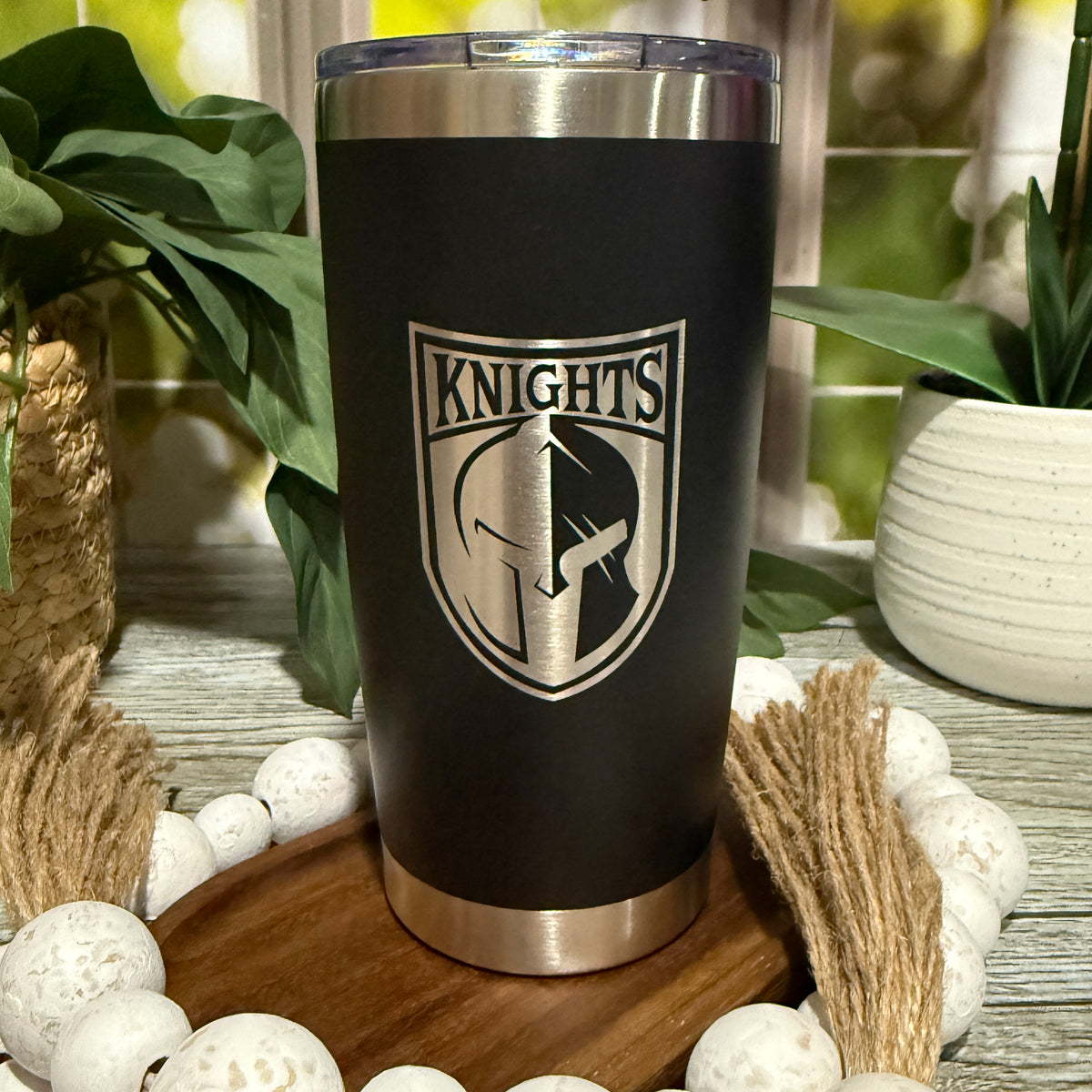 Black 20oz stainless steel tumbler engraved with Canandaigua Knights hockey team logo, staged with wood beads and greenery.