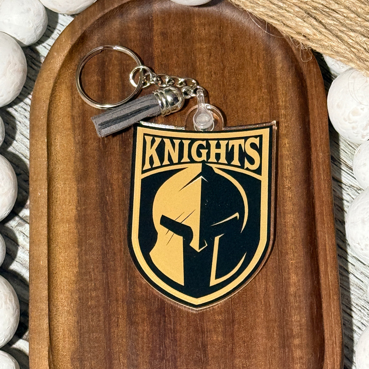 Acrylic keychain featuring the Canandaigua Knights logo, UV printed with optional gray and black tassel, displayed on a wooden tray with decorative beads.