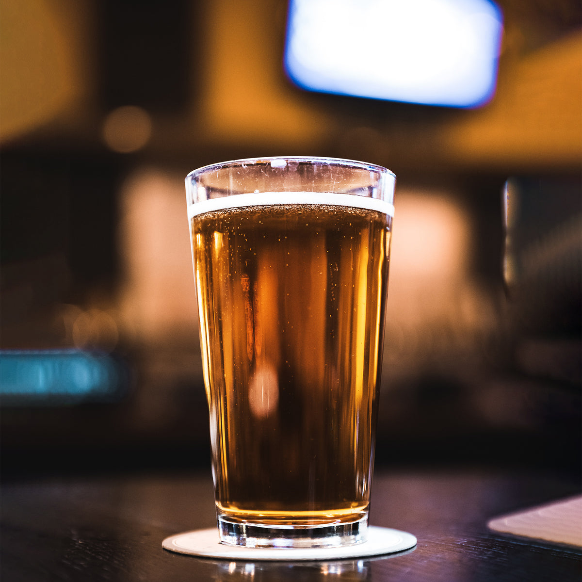 Pint glass engraved with beer quote, placed next to bottle opener and snacks