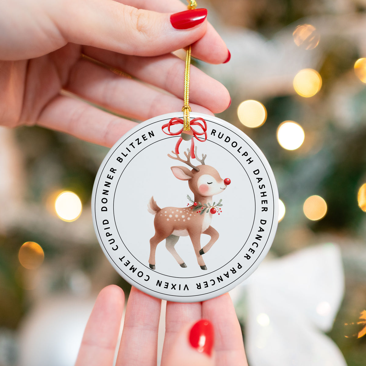 Rudolph reindeer ceramic Christmas ornament with Santa’s sleigh team names around the border, held in front of a decorated tree