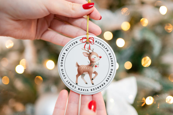 Rudolph reindeer ceramic Christmas ornament with Santa’s sleigh team names around the border, held in front of a decorated tree